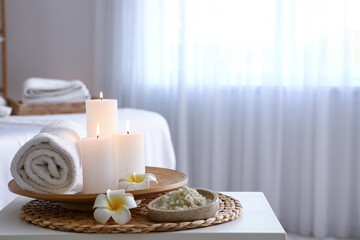 Spa composition with burning candles and flowers on table in salon, closeup