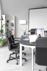 Interior of modern conference hall with shelving units, screen board, armchairs and table