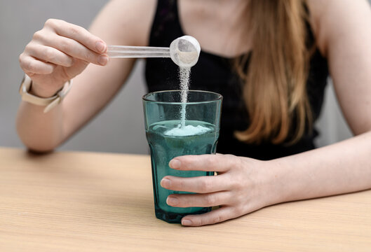 A woman dissolves a scoop of creatine powder in water to drink.