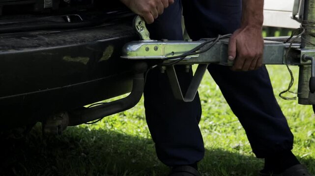 Man attaching trailer and safety rope to towbar of passenger car in summer, close-up, industry