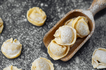 Wooden scoop with flour covered raw cappelletti pasta on dark background