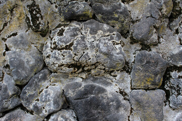 Close up of natural stone wall. Rough surface of stacked stones background. Cracked stones texture. Green moss and white lichen on natural stones.