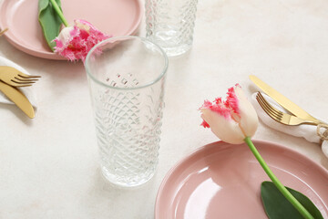 Beautiful table setting with pink plates, glasses, cutlery and flowers on light background, closeup