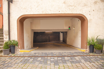 Entrance to an underground parking garage with cobblestone pavement, potted plants, and a green traffic light signal