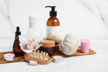 Set of spa supplies with different cosmetic products, herbal bags, massage brush and burning candles on white background