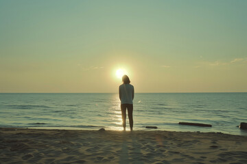 Fototapeta premium Woman standing on a beach and looking at the sunset