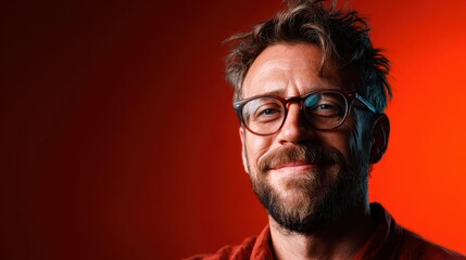 A smiling man with glasses stands against a warm red backdrop, capturing the essence of joy and confidence, perfect for representation of human emotion and personality.