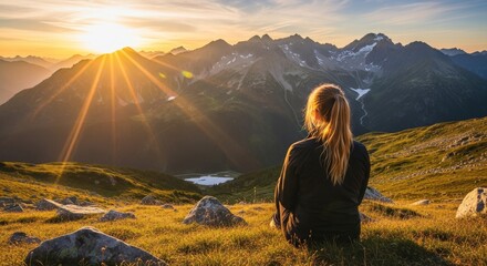 Woman admiring a breathtaking mountain sunrise from a grassy viewpoint