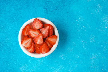 bowl of fresh sliced strawberries on blue background