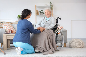 Young African-American female medical worker with elderly woman on wheelchair in nursing home