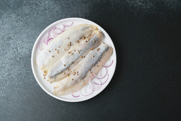 Marinated herring fillets with coriander seeds and onion on white plate over dark background