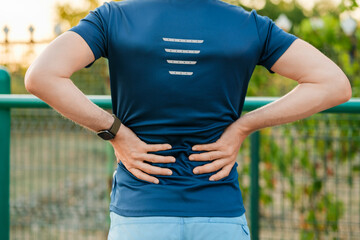 Fototapeta premium Person stretching near park during evening to relieve back pain while wearing a fitness shirt in a relaxed setting.
