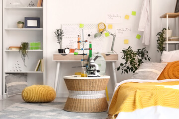 Modern microscope and chemical flasks on wicker table in stylish teenager's room