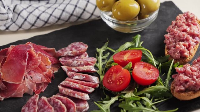 Snack plate beef tartar, cherry tomatoes, green olives and fuet sausage, jamon. Wine snack.