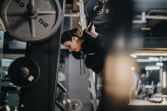 Focused woman lifting weights with barbell during a squat exercise in a contemporary gym. The environment emphasizes strength training and fitness dedication.