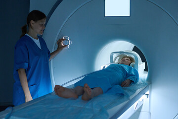 Caucasian middle aged woman operating MRI scanner while Caucasian child lying on examination table...