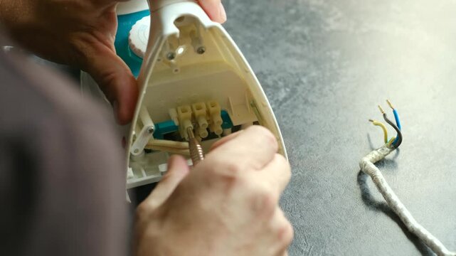 Close up technician hands meticulously connecting electrical cable to terminals of iron, demonstrating process appliance repair. Technician connecting electrical cable to iron terminals