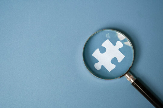 A magnifying glass focuses on a white puzzle piece against a blue background, symbolizing problem-solving or searching for solutions.