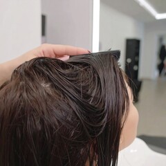 Fototapeta premium A person's wet dark brown hair is being combed by a hand in a salon setting.