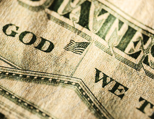 Close-up captures layered one-hundred-dollar bills highlighting In God We Trust and American flag design, with shallow depth of field focusing on foreground bill. Green and beige tones of USD notes