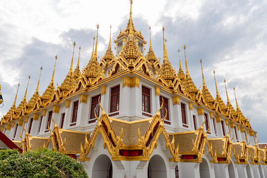 Golden spires of loha prasat at wat ratchanatdaram in bangkok, thailand, ornate buddhist temple against a cloudy sky