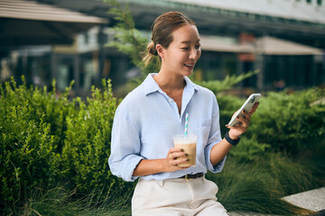 Asian Woman Enjoying Coffee While Using Smartphone in Outdoor Cafe