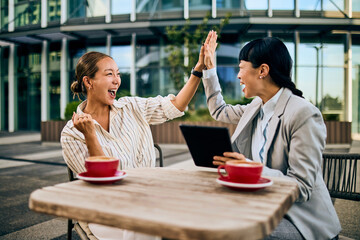 Two Happy Women Celebrating Teamwork at Outdoor Cafe with High Five