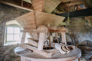 Close-up view of a traditional wooden grain mill inside a rustic windmill, with wooden clogs resting on the mill and a soft light entering through a window. © Raivo