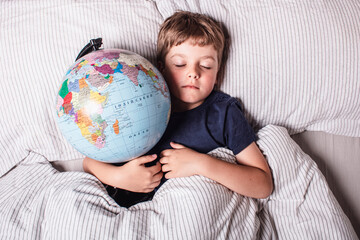 Peaceful boy sleeping with globe in bed, representing childhood dreams, imagination, innocence, hope for the future, and the vision of a better connected world full of possibilities.
