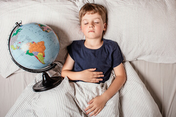 Child resting in bed with a globe, symbolizing learning, geography, global education, curiosity, and the importance of knowledge for the younger generation in a connected world.
