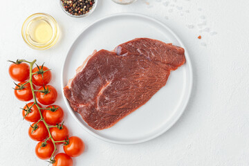 Raw beef steak on white plate with tomatoes and cooking ingredients