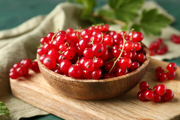 Wooden cutting board and bowl with fresh red currants on green grunge background, closeup