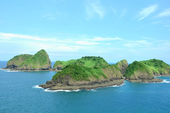 A beautiful coastal landscape at Bedil Island, Banyuwangi, Indonesia. Lush green hills covered in dense vegetation rise dramatically from the clear blue ocean