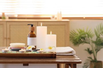 Composition with spa accessories, bottle of cosmetic product and burning candles on wooden table in salon