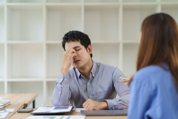 Asian businessman suffering from headache and stress at work while talking with a female colleague