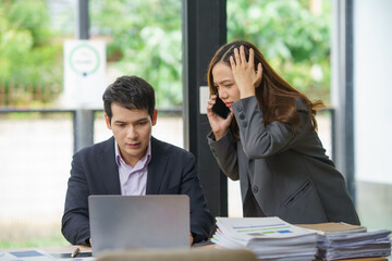 Businesswoman getting stressed receiving bad news while talking on the phone, businessman working with laptop in office