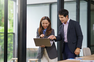 Businesswoman holding a laptop and engaging in a discussion with a businessman inside a modern office, fostering collaboration and teamwork