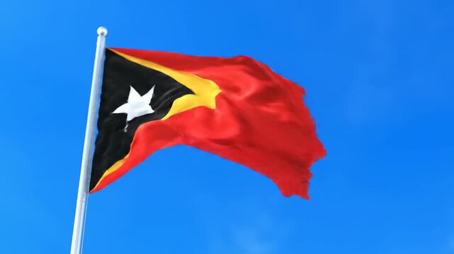 The flag of East Timor waving against a bright blue sky