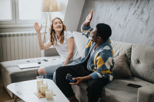 Two friends sharing a joyful moment, sitting on a sofa, expressing happiness through a high-five gesture, in a cozy and relaxing home atmosphere. - Powered by Adobe