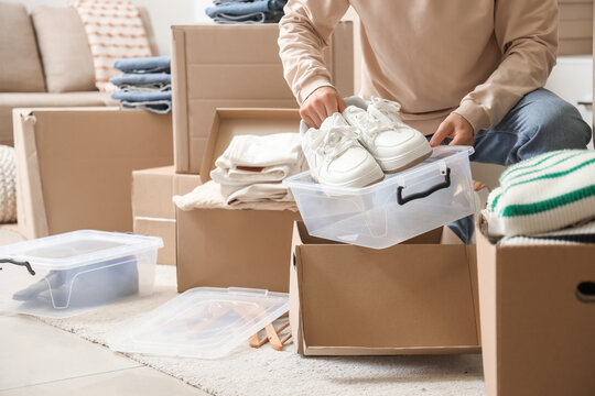 Young man with wardrobe boxes putting sneakers into container in dressing room - Powered by Adobe