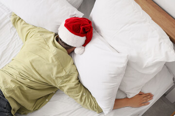 Drunk young man with Santa hat sleeping in bedroom after New Year party, top view