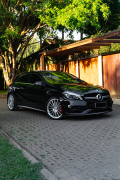 Black Mercedes A45 AMG hot hatch at golden hour, German performance car under a tree at sunset.

