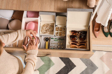 Young woman putting on ring near organized jewelry and underwear in wardrobe, top view