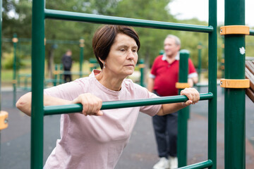 Obraz premium elderly woman doing exercises on a horizontal bar at an outdoor sports ground
