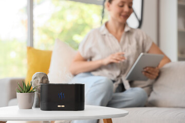 Fototapeta na wymiar Air humidifier on table against woman using tablet computer at home, closeup