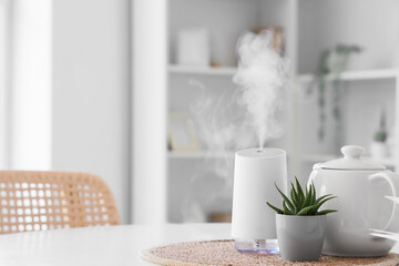 Air humidifier with plant and teapot on dining table in room, closeup