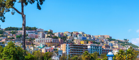 A wide panoramic view of the colorful buildings on Vomero hill in Naples, Italy. The historic Castel Sant'Elmo is visible at the top of the cityscape.