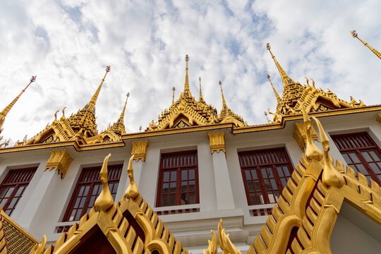 Majestic golden roof details and spires of Loha Prasat Buddhist temple in Bangkok Thailand with traditional architecture and cloudy sky background
