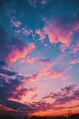 Fototapeta premium Vibrant sunset hues paint the sky with pink, orange, and blue clouds, silhouetted buildings below