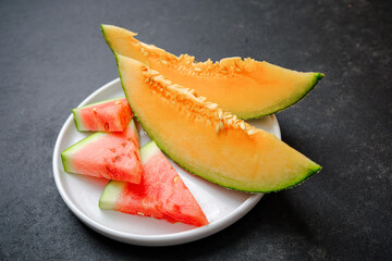 Juicy melon slices and watermelon pieces on a white plate with a dark backdrop. Refreshing summer fruits.